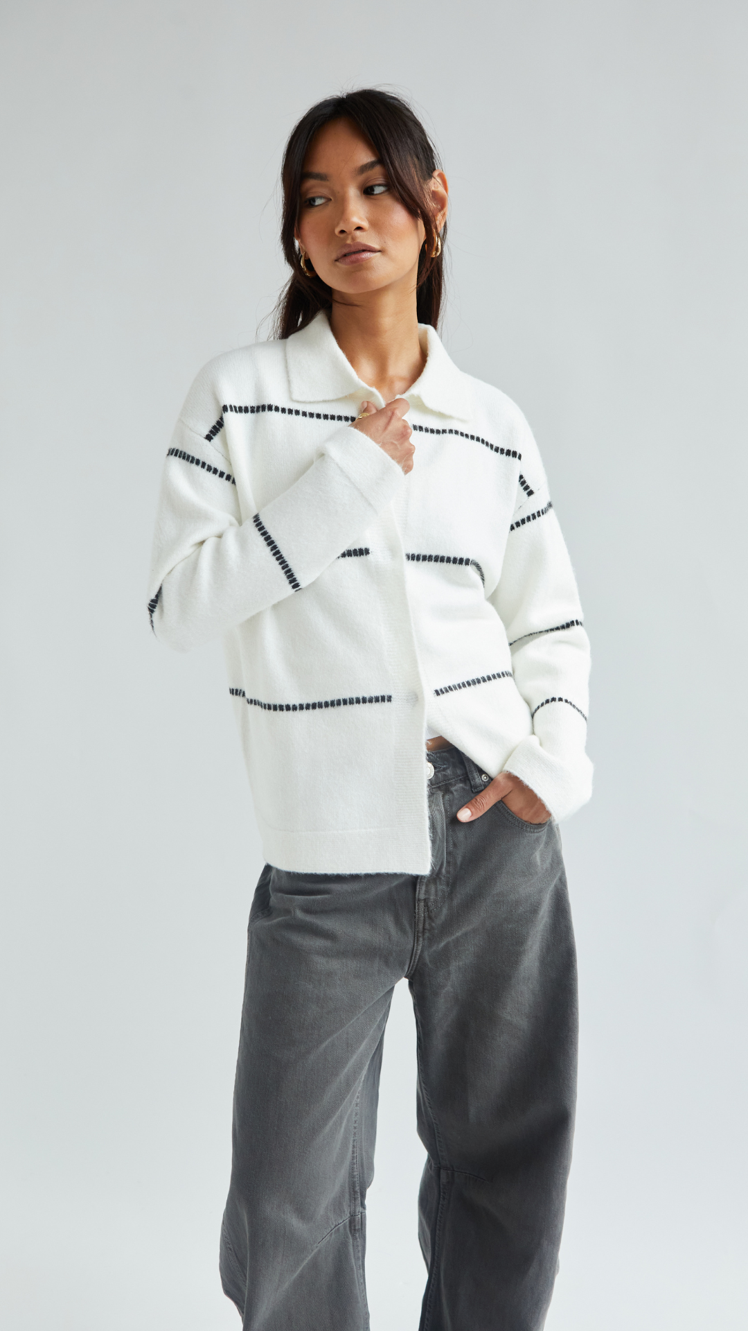 white button-up cardigan with black horizontal stitch detailing, styled with high-waisted wide-leg grey jeans, accessorized with gold hoop earrings
