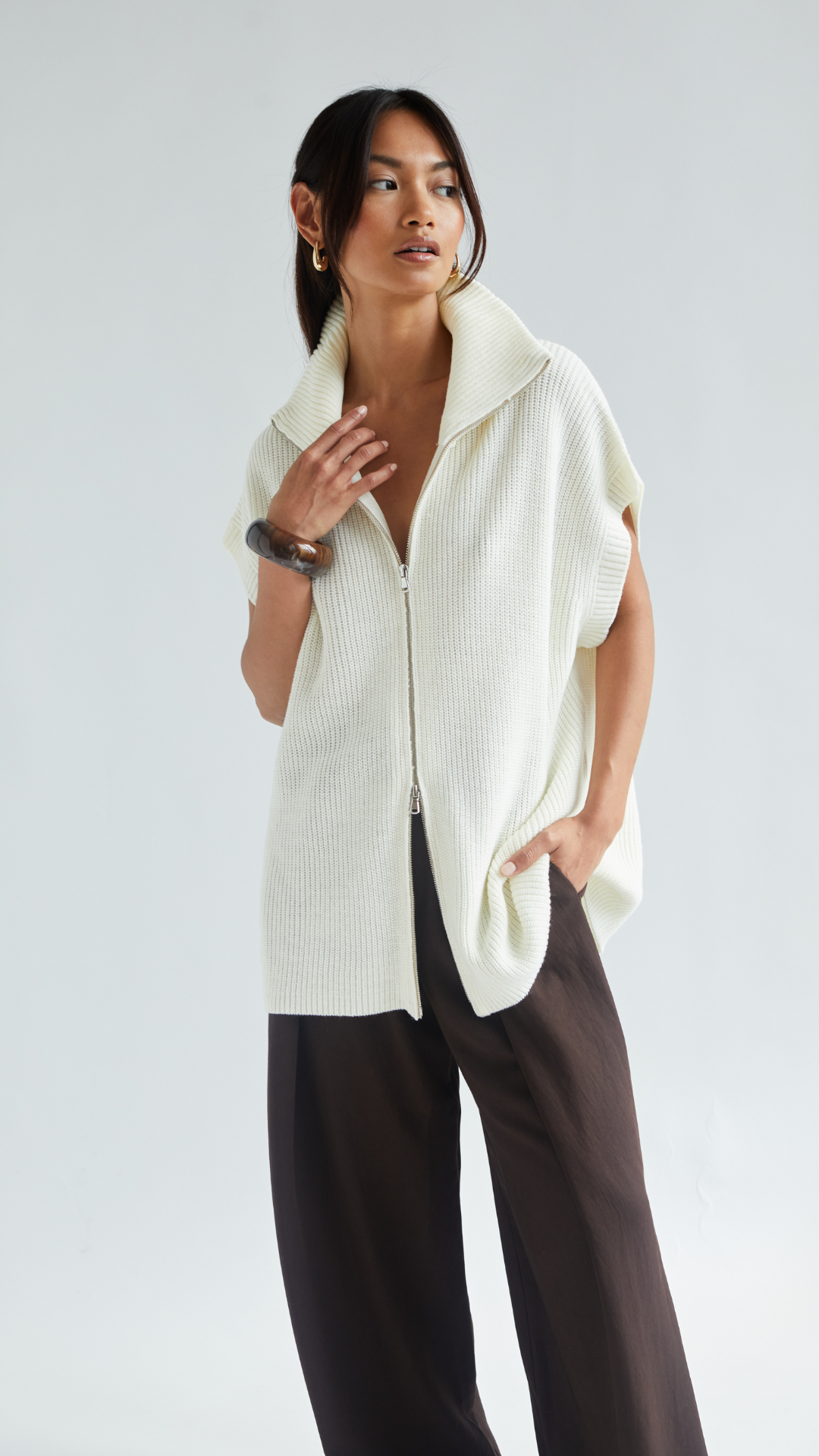 cream zip-up knitted sweater with a high collar and short sleeves, paired with dark brown wide-leg trousers