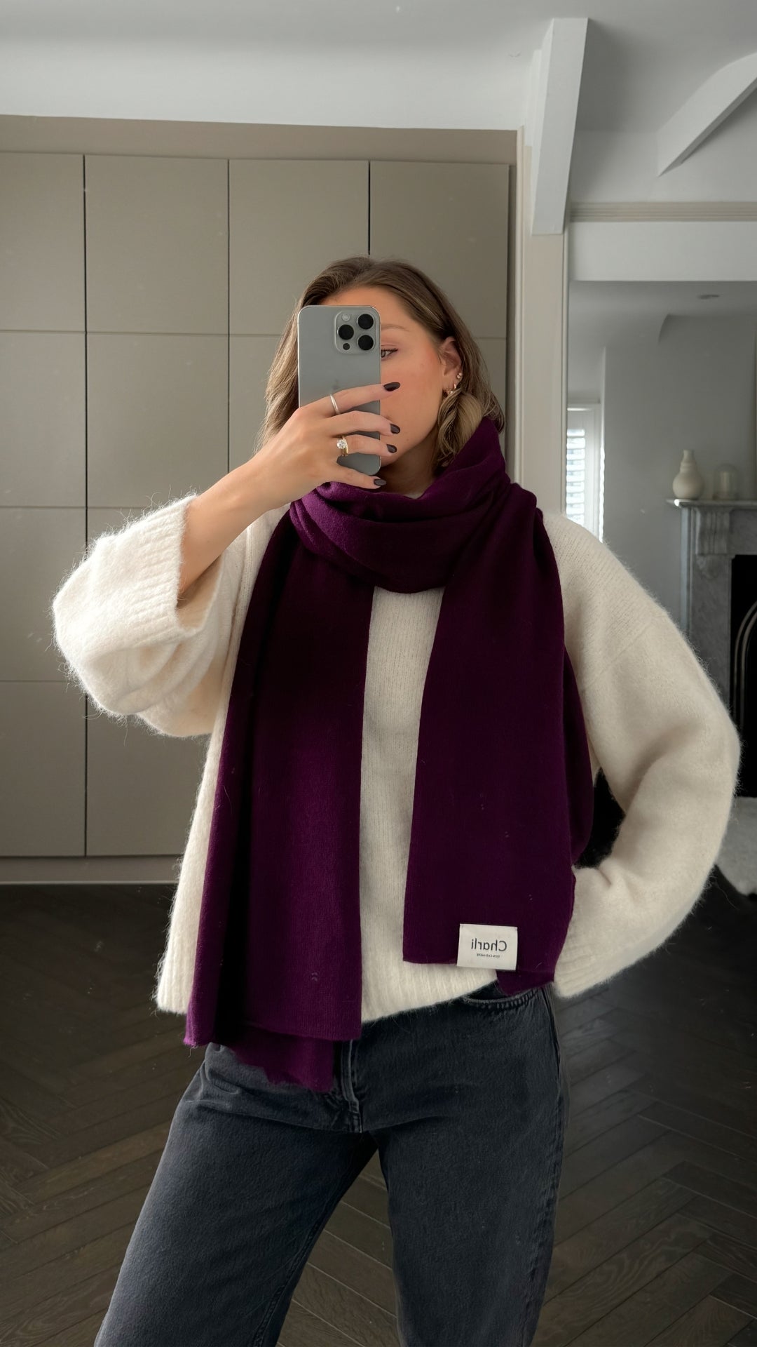 cozy ivory sweater paired with dark grey jeans, styled with a deep purple scarf featuring a small logo tag