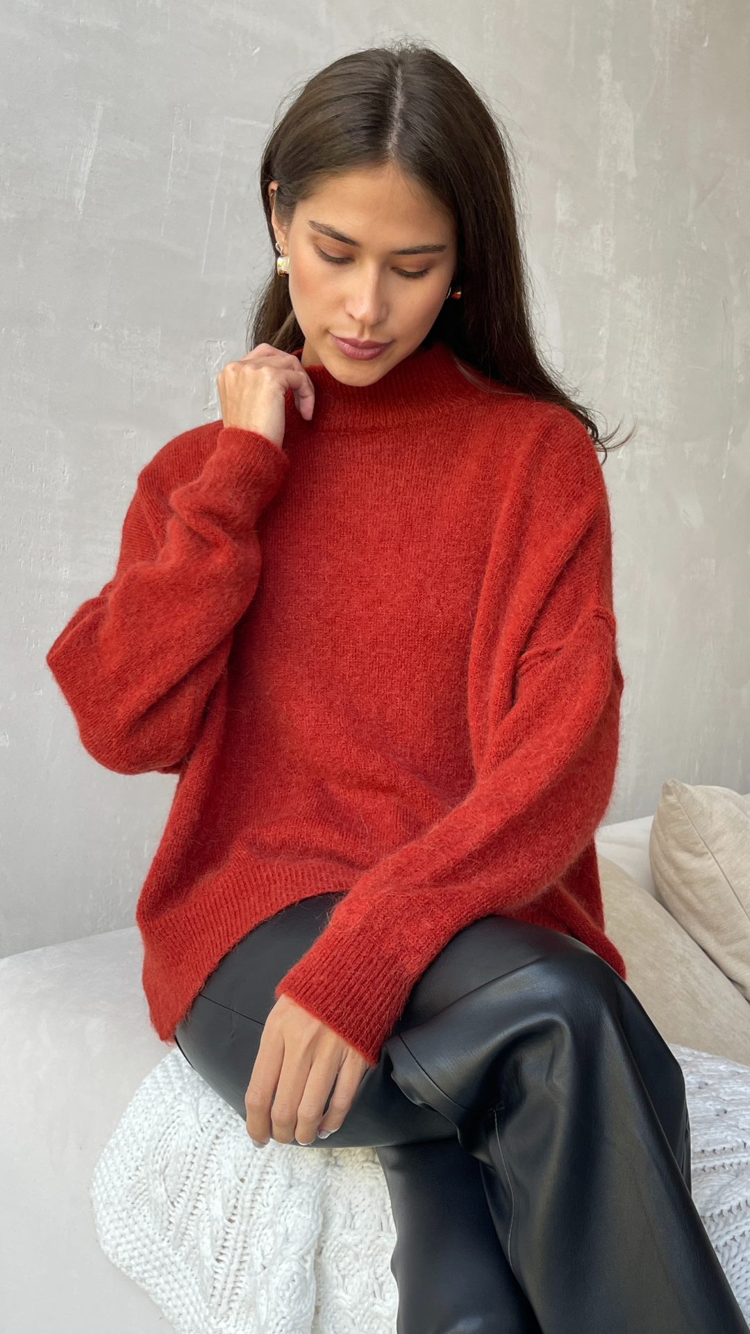 Woman wearing a red turtleneck sweater with a relaxed fit and ribbed cuffs, paired with black leather trousers for a stylish and cozy look.