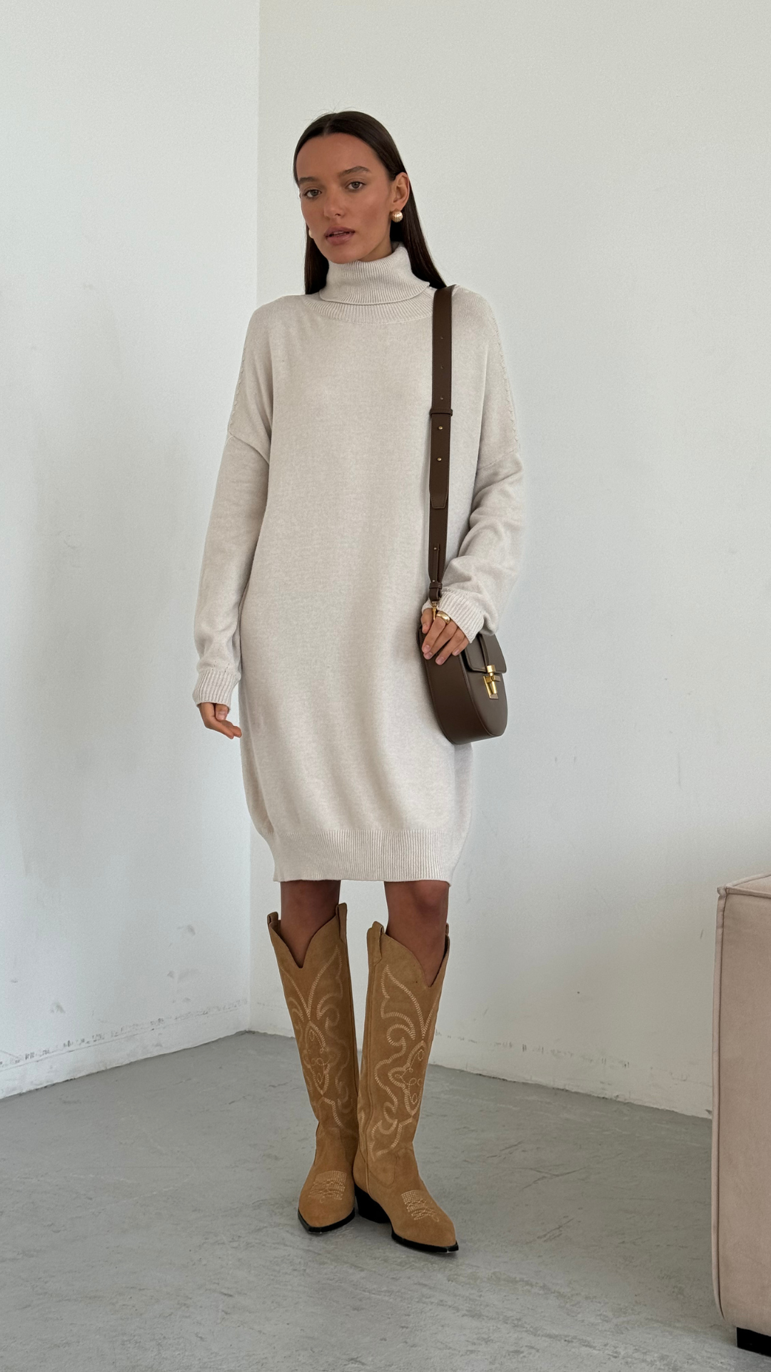 cream turtleneck sweater dress styled with camel suede knee-high cowboy boots, accessorized with a brown leather crossbody bag