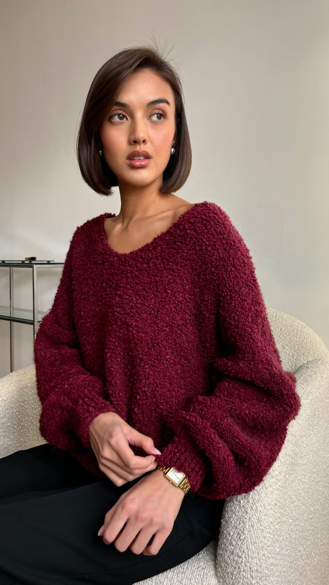 Cosy burgundy textured sweater with voluminous sleeves, styled with black trousers and accessorised with a gold wristwatch and pearl earrings