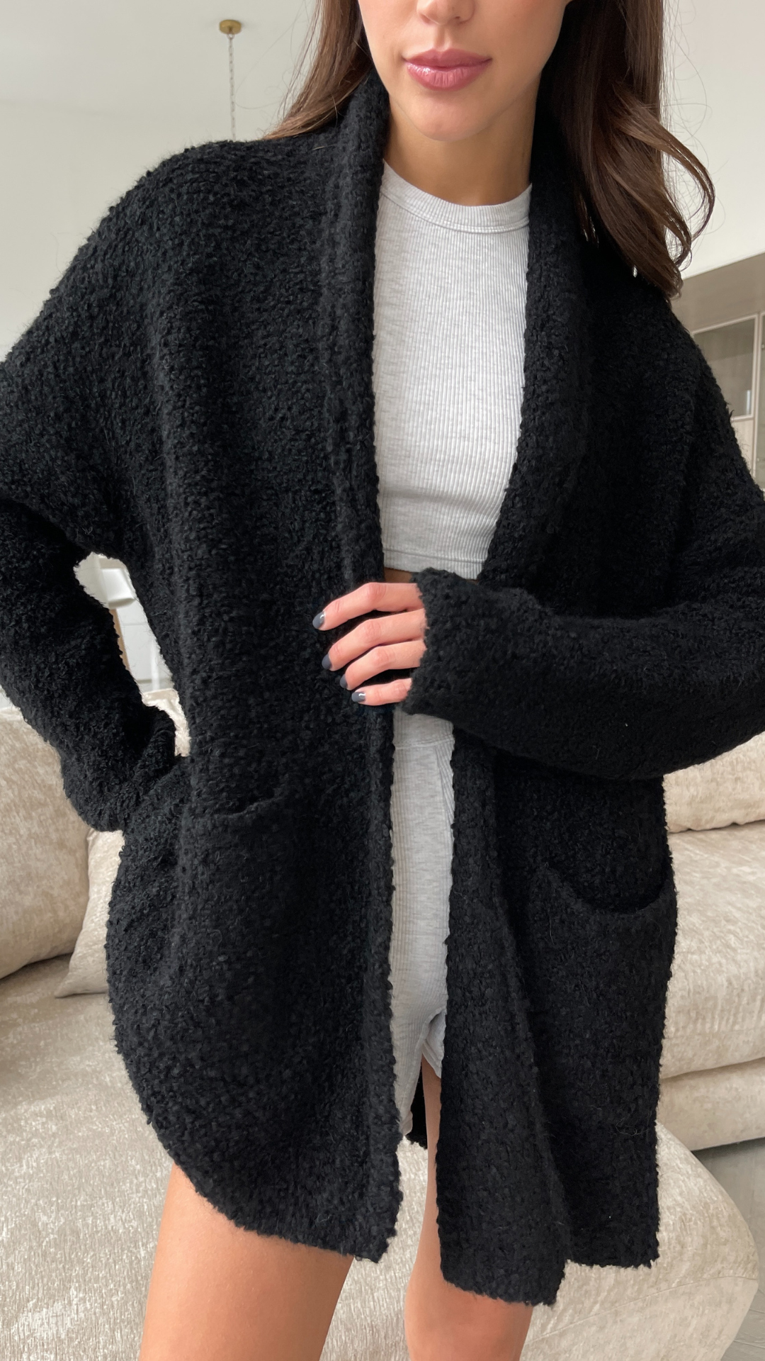 black oversized fleece cardigan with an open front and large pockets, styled over a white ribbed top