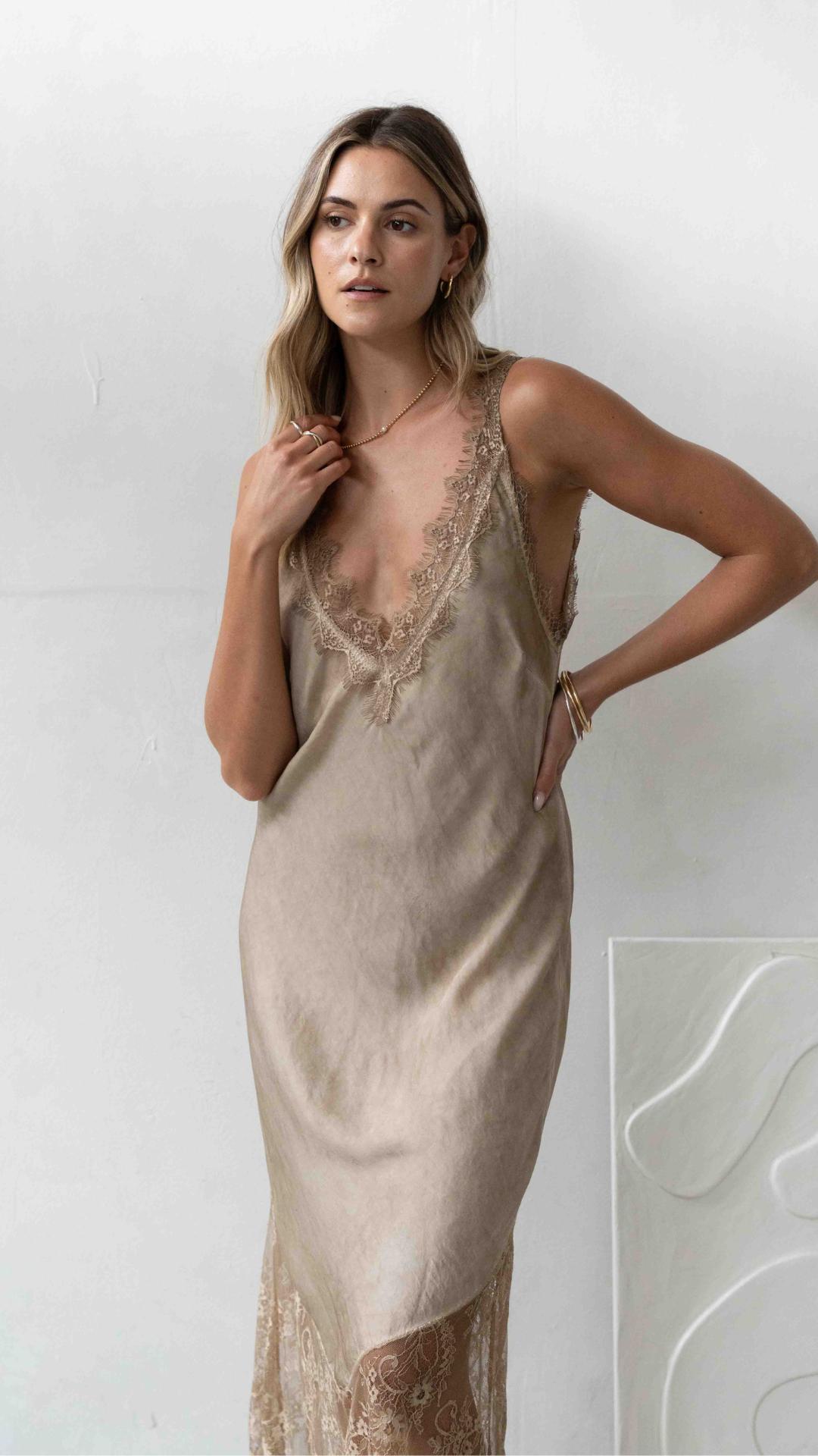 beige slip dress featuring a delicate lace-trimmed plunging neckline and a sheer lace hem, styled with gold jewellery