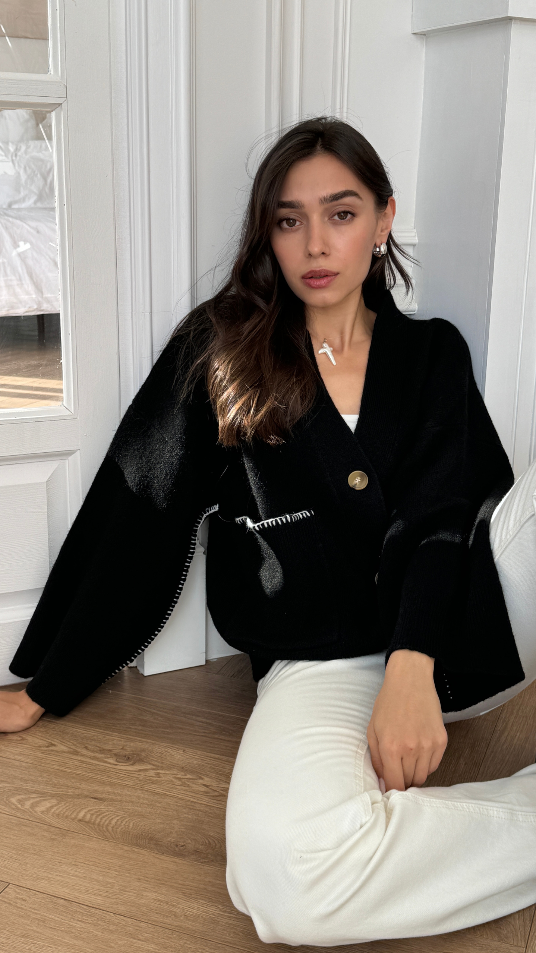 black oversized cardigan with a large button and white stitching details, paired with white trousers