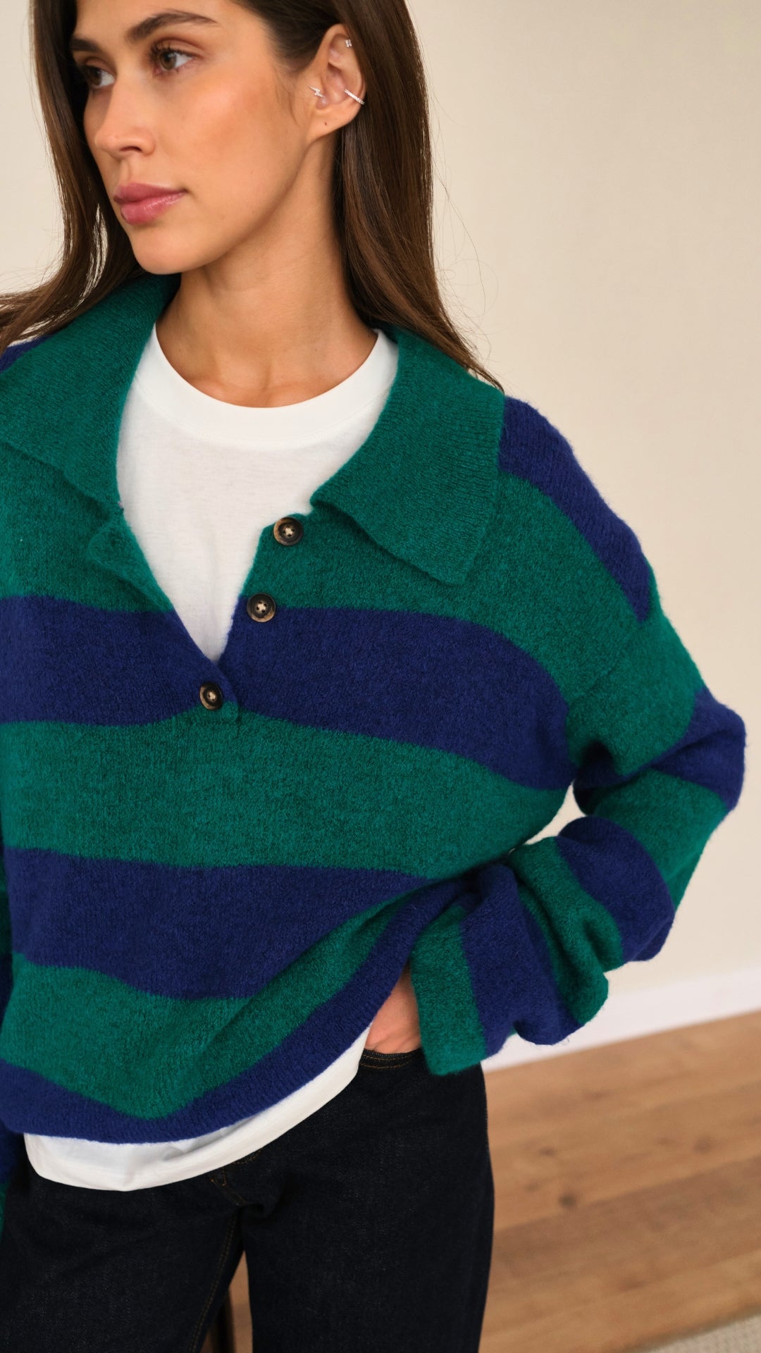green and navy blue striped knit sweater with a buttoned collar, layered over a white t-shirt and paired with dark jeans