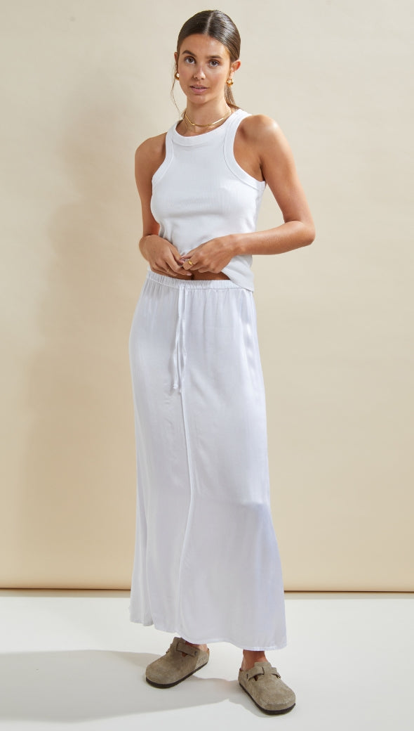 white sleeveless ribbed tank top paired with a white drawstring maxi skirt, styled with beige suede slip-on shoes