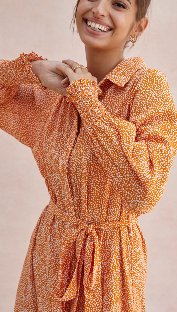 orange and white patterned collared dress with long sleeves and a cinched tie-waist