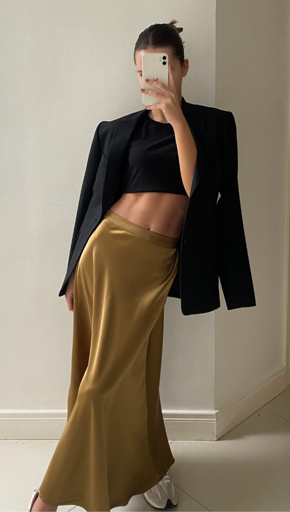 black crop top and a gold satin maxi skirt, paired with a black blazer draped over her shoulders.
