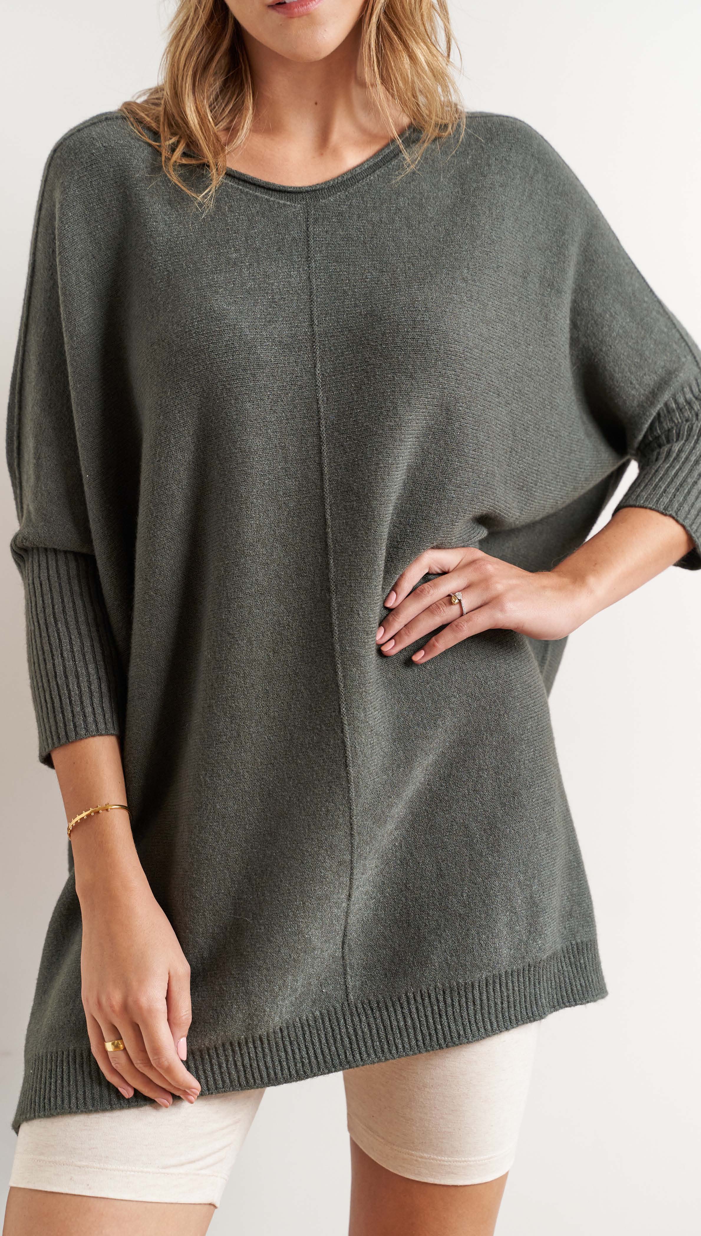 oversized dark olive green knit sweater with a seam detail and ribbed sleeves, styled with beige cycling shorts