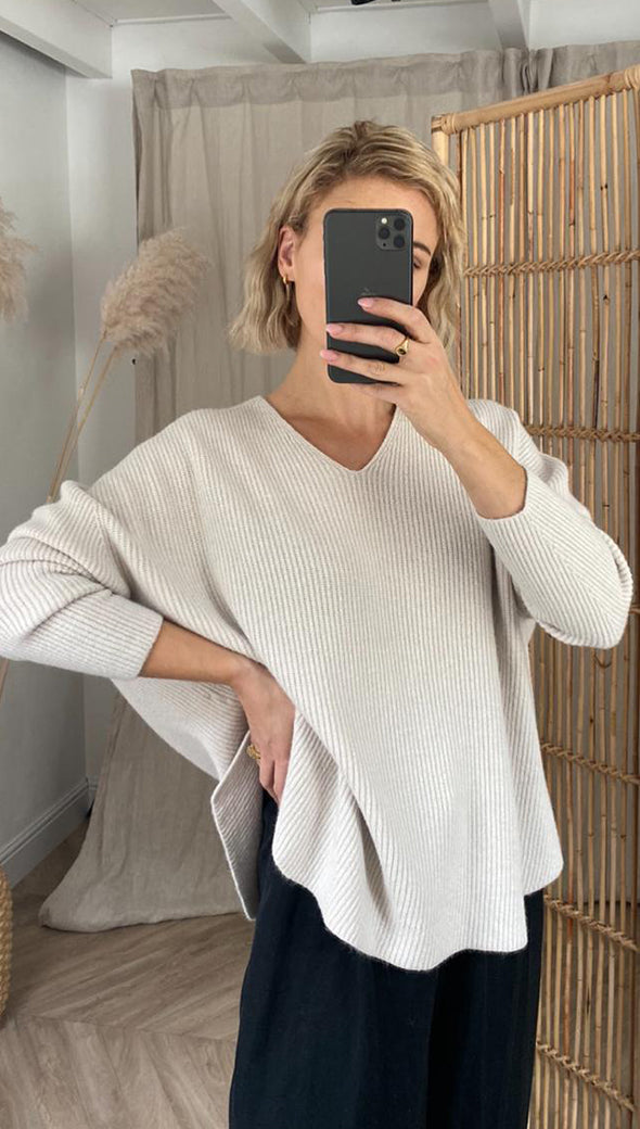 Woman wearing a cream oversized ribbed sweater with a V-neckline and wide sleeves, paired with black trousers