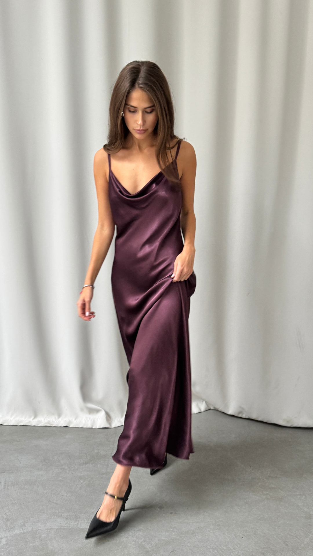 plum satin slip dress featuring a draped cowl neckline and thin spaghetti straps, paired with black pointed-toe heels