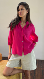 vibrant pink textured button-up shirt with rolled-up sleeves, paired with beige linen shorts