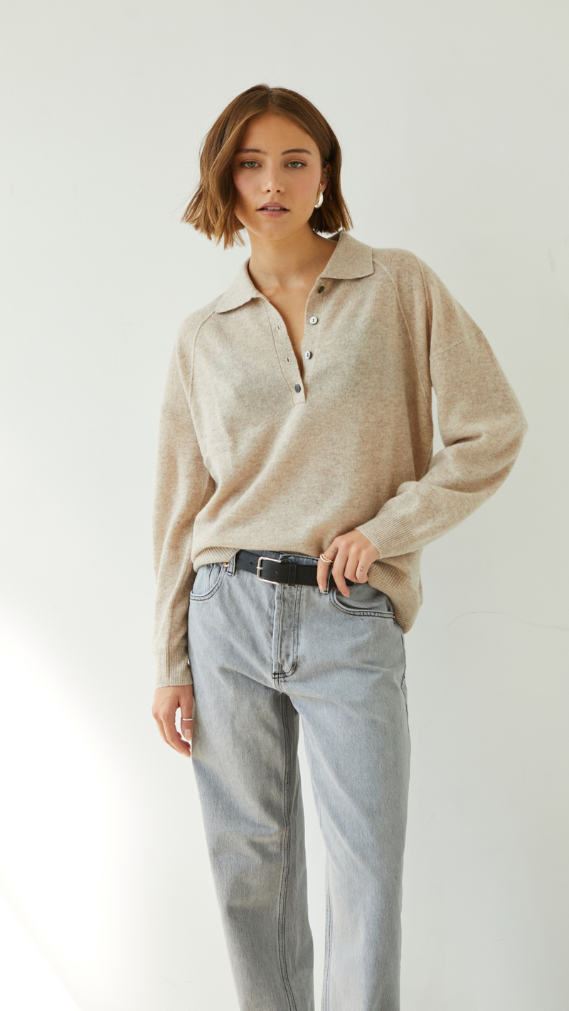 beige collared sweater with button details, paired with light grey jeans and a black belt