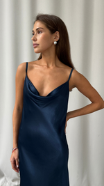 navy blue satin slip dress with a draped cowl neckline and thin spaghetti straps, styled with statement pearl earrings
