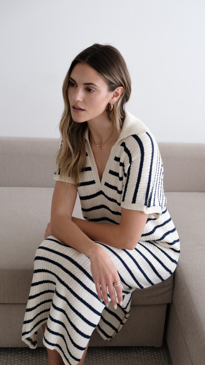 Woman wearing a cream and navy striped knit dress with short sleeves and a V-neck collar