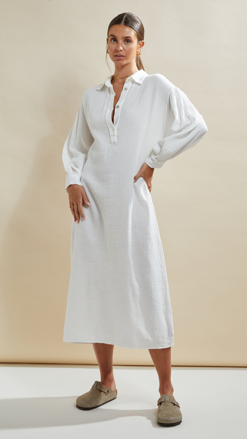 Woman wearing a white long-sleeve midi dress with a button-down collar, featuring a relaxed fit and textured fabric, styled with beige slip-on shoes