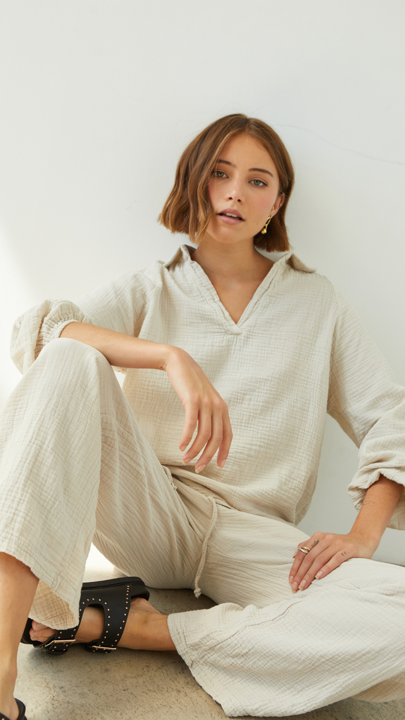 beige textured two-piece outfit featuring a relaxed-fit collared blouse and drawstring wide-leg trousers, accessorized with gold earrings and black studded sandals