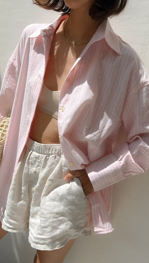 light pink striped button-up shirt over a beige crop top, paired with beige linen shorts