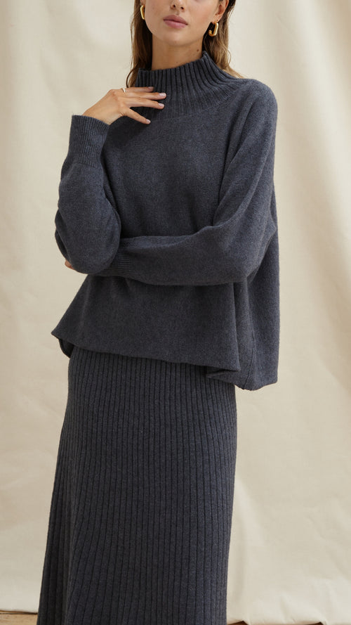 charcoal grey knit set featuring a high-neck oversized sweater and a ribbed midi skirt, accessorized with gold earrings