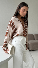 silk button-up shirt with a brown abstract pattern, paired with white trousers and holding a cream clutch