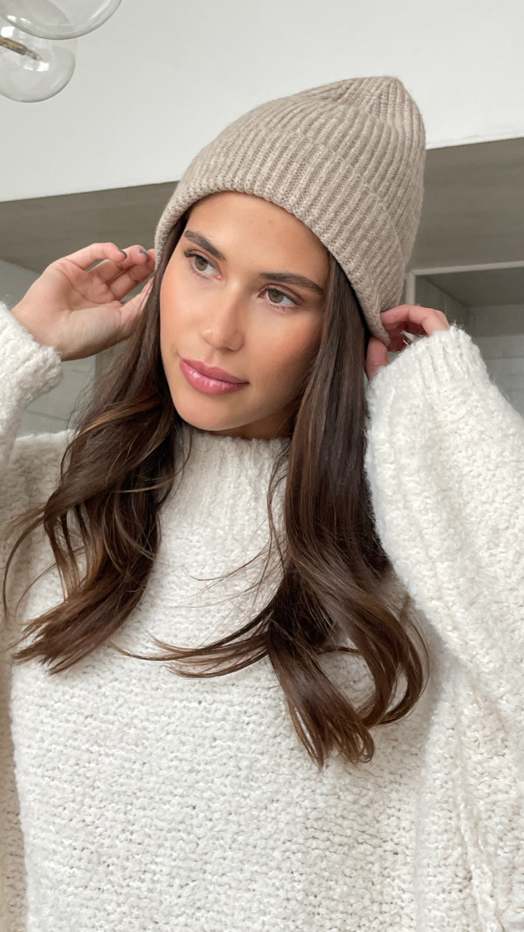 cream textured jumper, adjusting her soft beige knit beanie