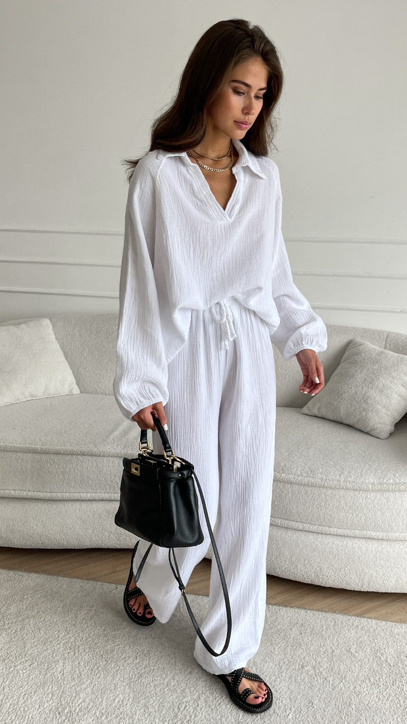 white textured co-ord set featuring a loose-fit collared blouse and drawstring wide-leg trousers, accessorized with a black leather handbag, layered gold necklaces, and black sandals