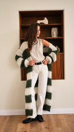 sleeveless beige top tucked into white high-waisted trousers with a black belt, styled with a long green and white striped knit cardigan and black loafers