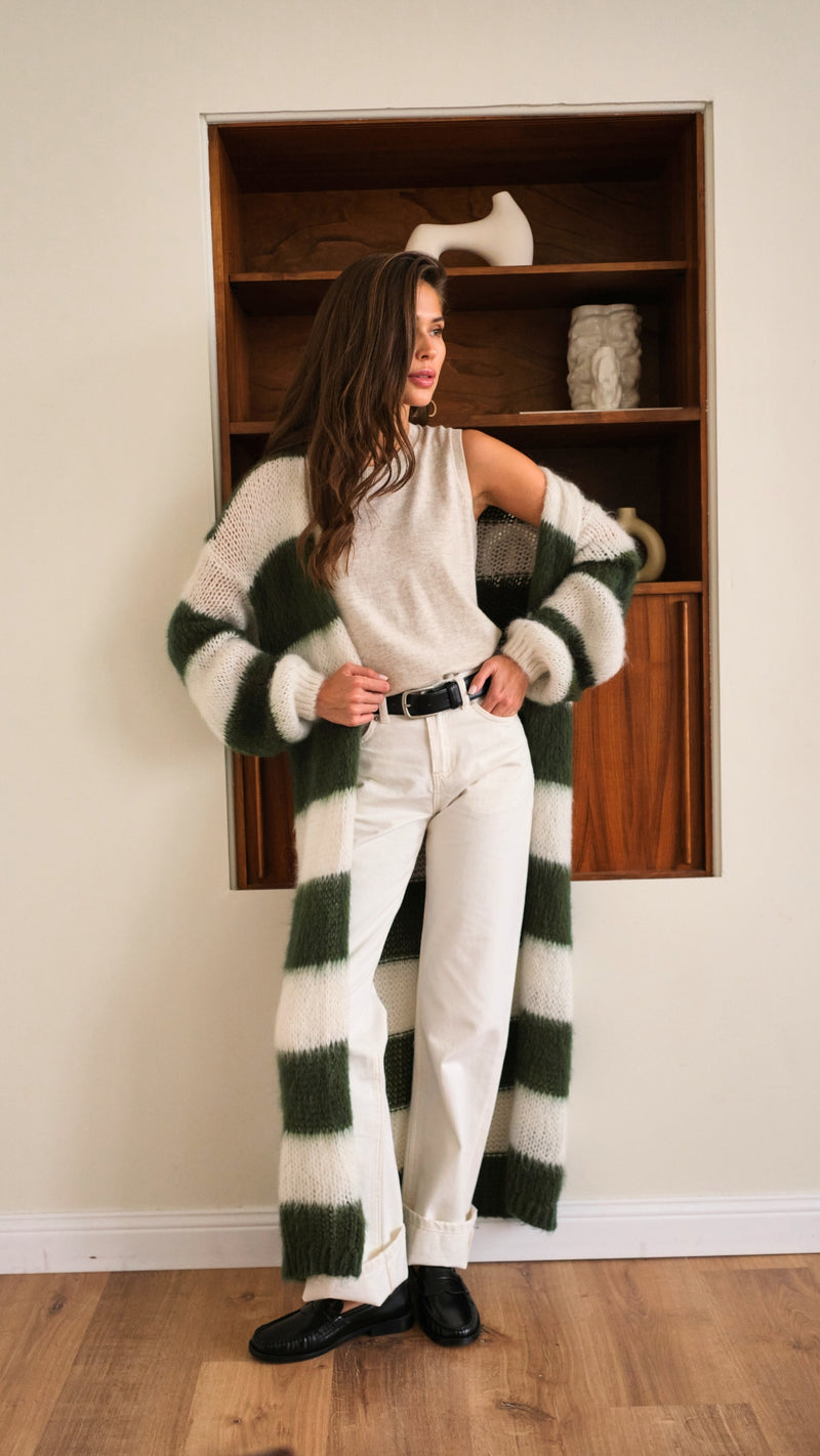 sleeveless beige top tucked into white high-waisted trousers with a black belt, styled with a long green and white striped knit cardigan and black loafers