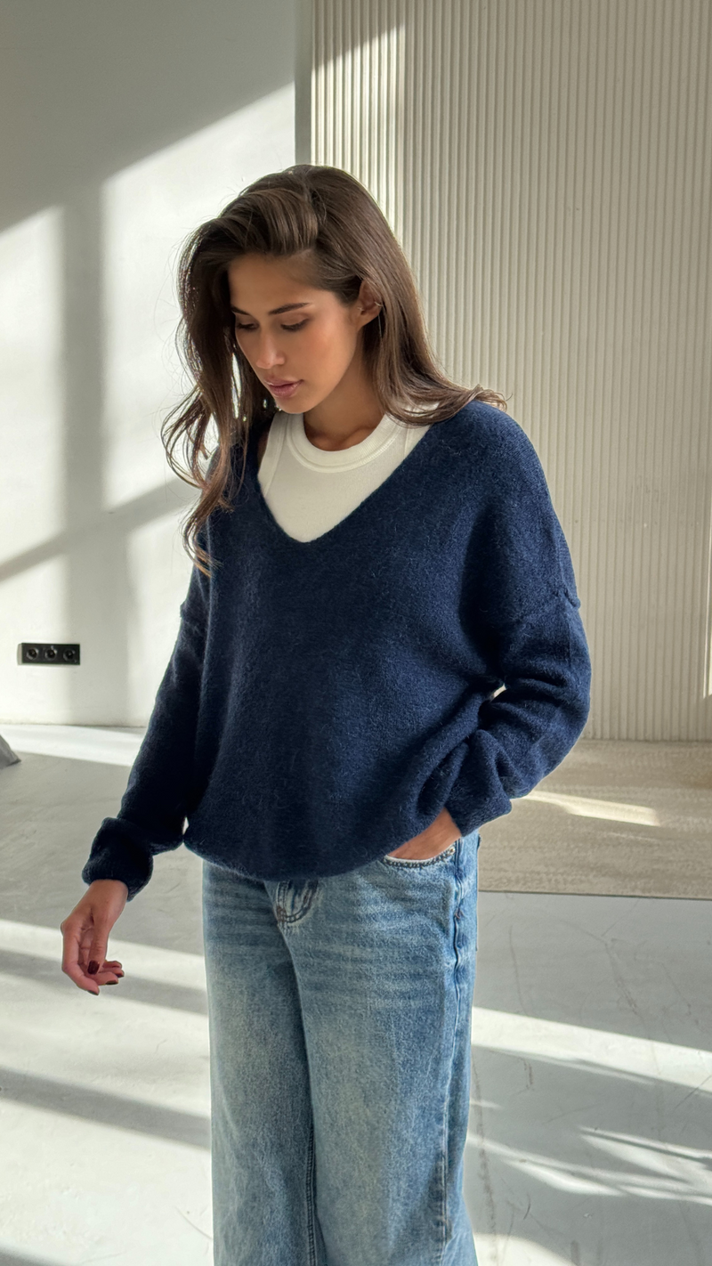 navy blue V-neck sweater layered over a white top, paired with light blue denim jeans
