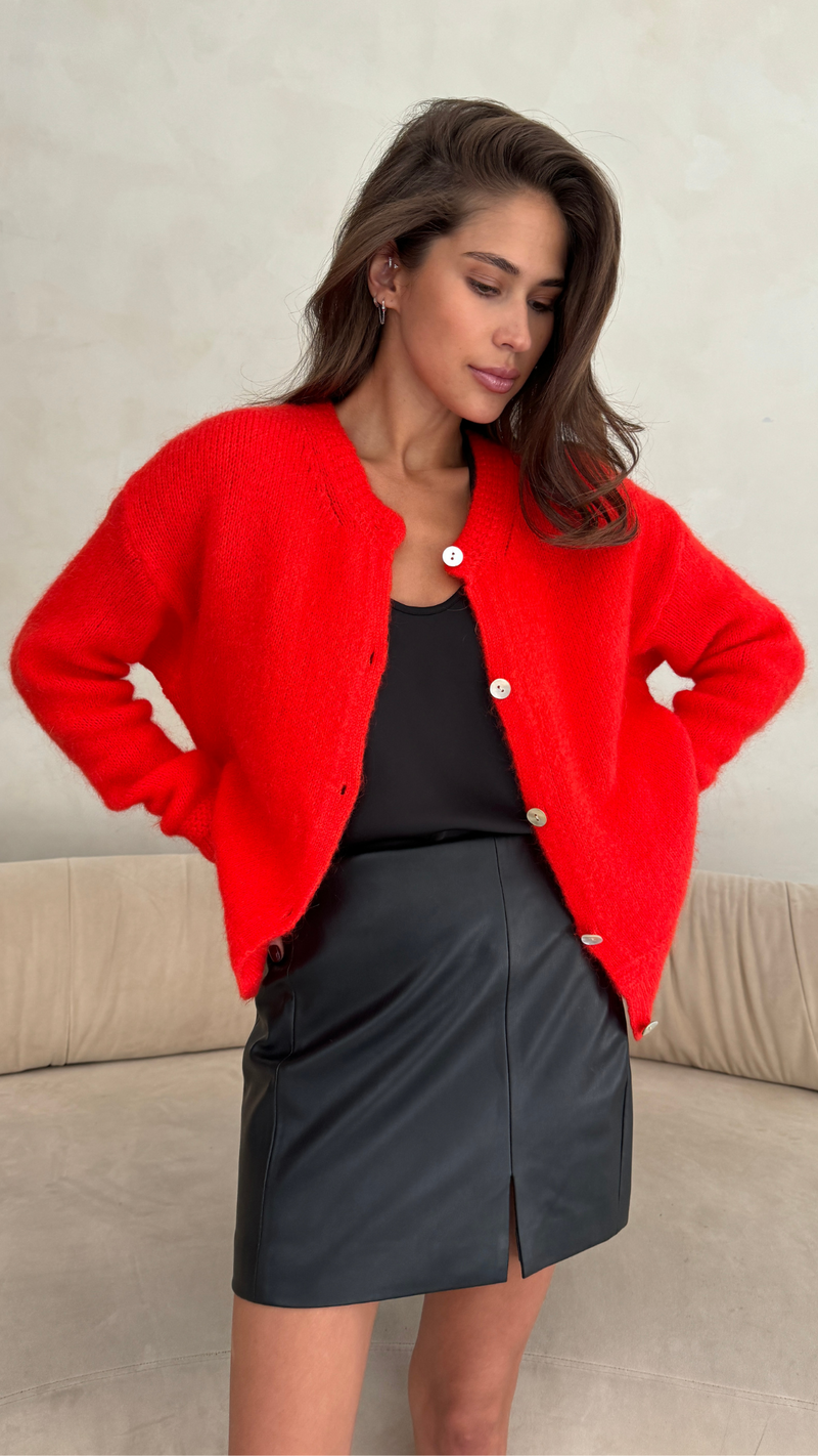 red cardigan with a button-up front over a black top, paired with a black leather mini skirt