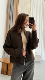 dark brown cropped zip-up cardigan over a beige top, paired with high-waisted black jeans