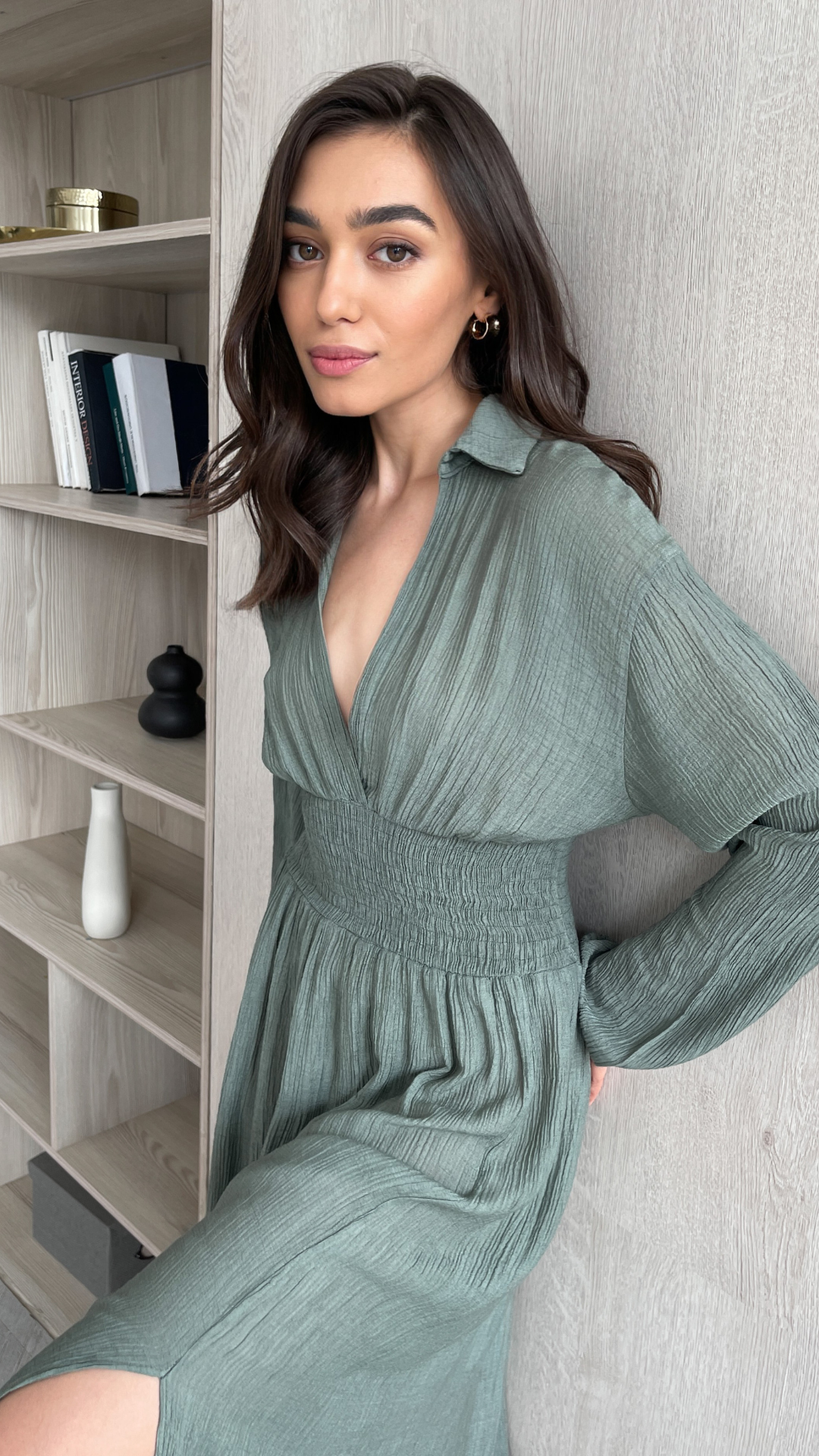 Woman in a sage green long-sleeve dress with a deep V-neckline and cinched waist