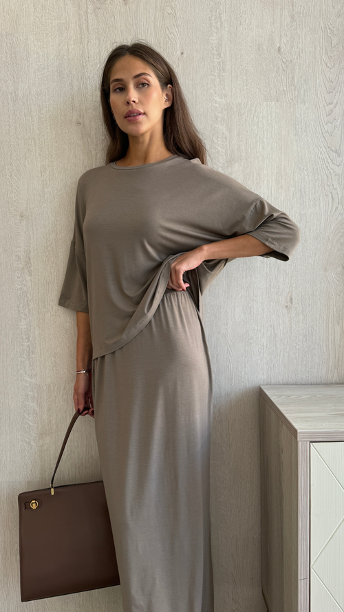 taupe loose-fitting top and skirt set with half sleeves, holding a brown leather handbag