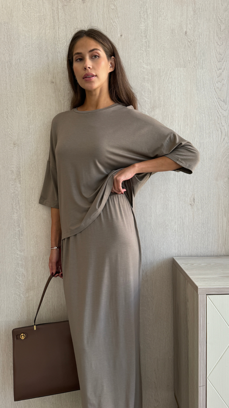 taupe loose-fitting top and skirt set with half sleeves, holding a brown leather handbag