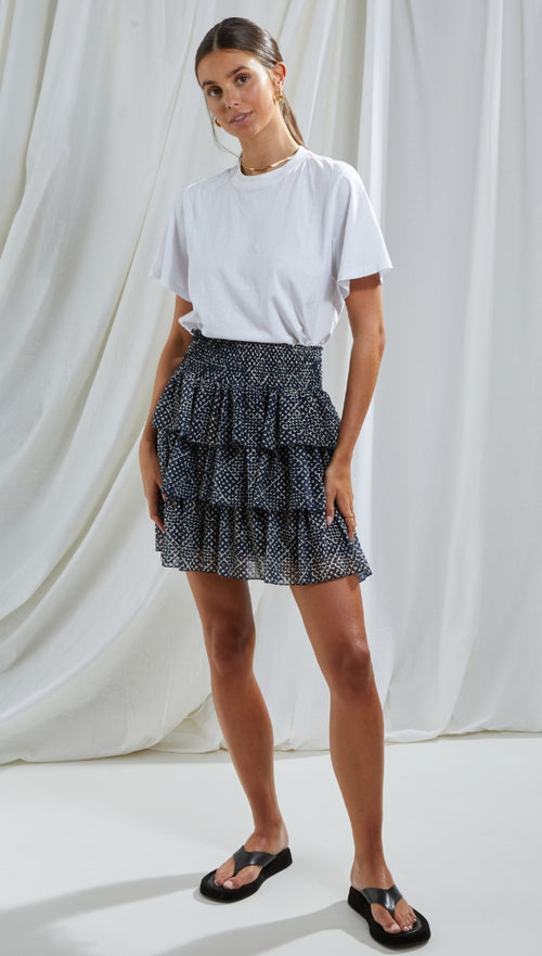 casual white t-shirt tucked into a black tiered ruffle mini skirt with a dotted pattern, paired with black sandals and minimal gold jewellery