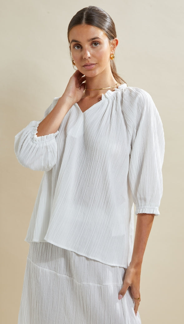 white flowy textured blouse with gathered details at the neckline and sleeves, paired with a matching skirt