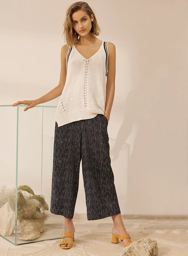 white sleeveless V-neck knit top with black stripe shoulder detailing, paired with wide-leg textured black trousers and yellow block-heeled sandals