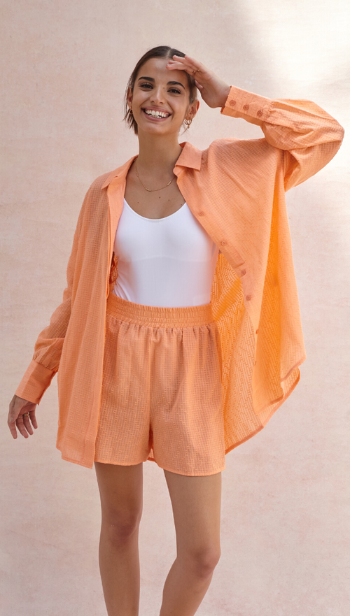 lightweight orange button-up shirt with matching shorts, styled over a white bodysuit