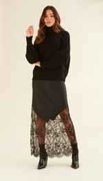 black ribbed high-neck sweater paired with a layered black skirt featuring lace detailing