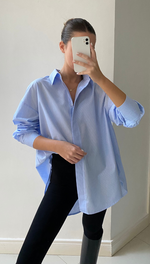 Woman wearing an oversized blue and white striped button-up shirt with black leggings and knee-high boots, creating a casual yet stylish look.