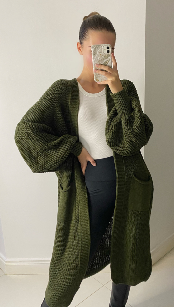 olive green chunky knit cardigan with oversized sleeves and front pockets, layered over a white ribbed top and paired with black high-waisted leggings