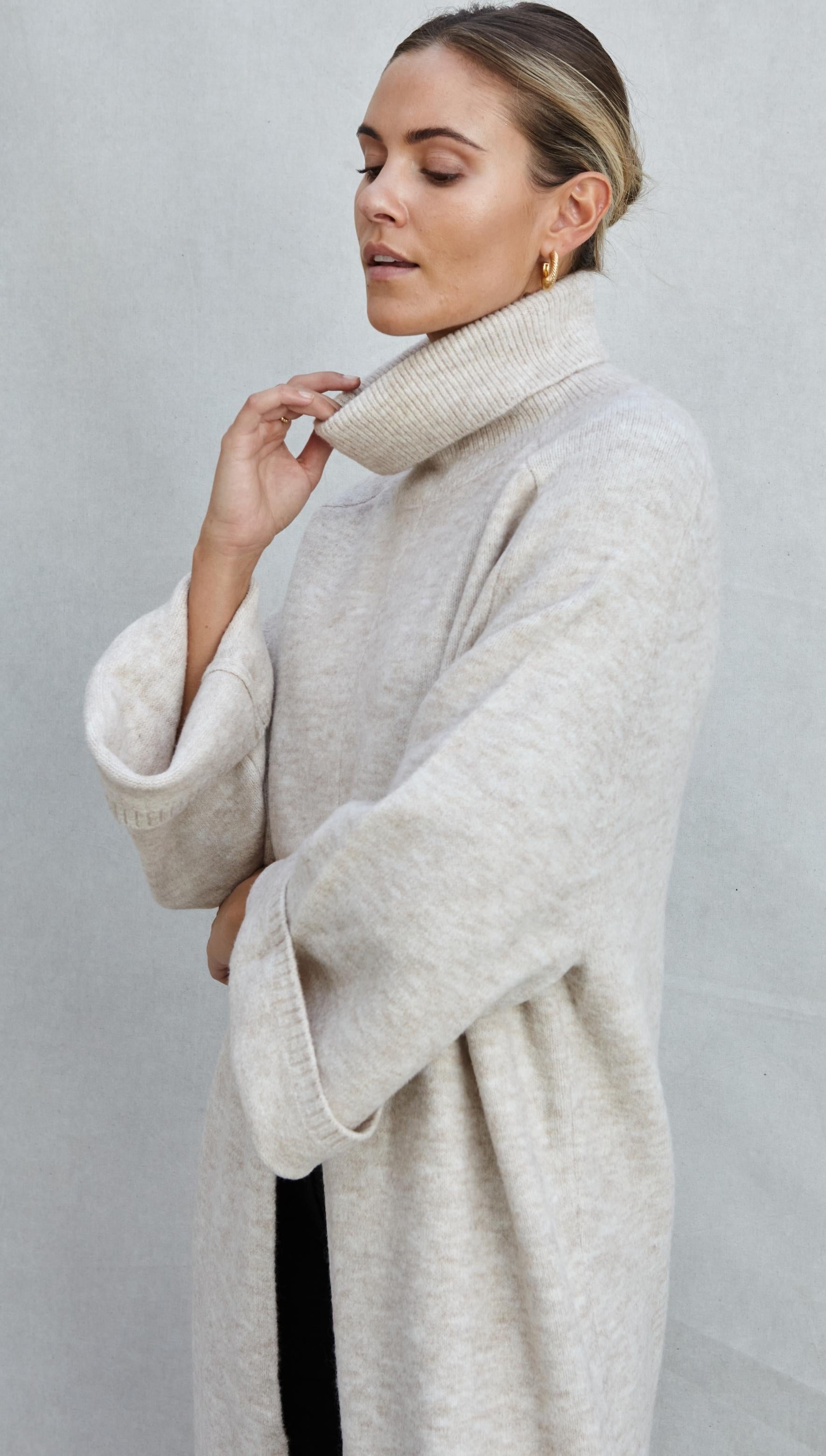 light beige oversized turtleneck sweater with wide sleeves, accessorized with gold hoop earrings,