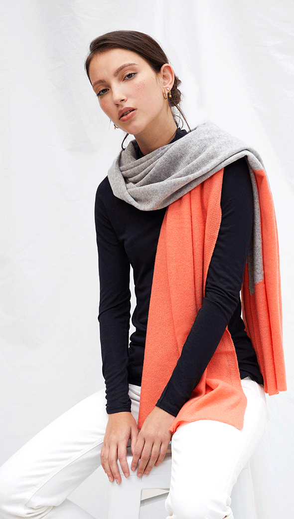 navy long-sleeve top paired with a grey and orange colour-blocked scarf, and white trousers