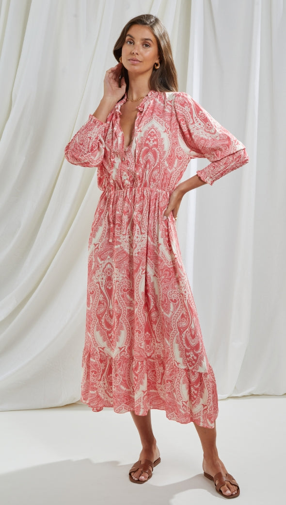 pink and white paisley-patterned midi dress with long sleeves, a cinched waist, and a tiered hem, styled with brown slide sandals