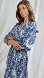 blue and white paisley-patterned midi dress with a collared neckline and long sleeves, accessorized with gold hoop earrings